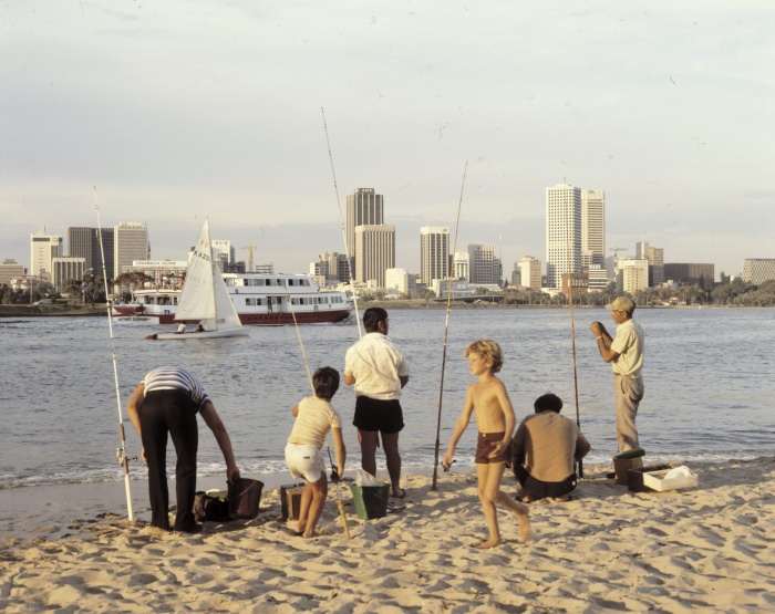 A family fishes on the banks of the swan river with East Perth apartment blocks seen on the other side