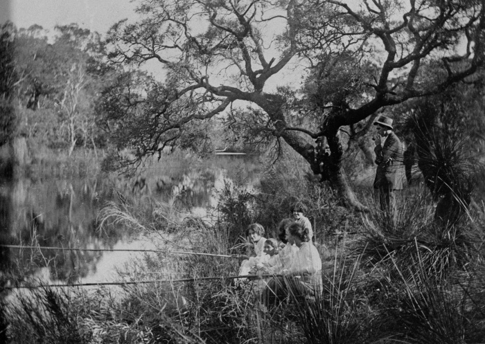 A family sits on a river bank with a couple of fishing rods in the water