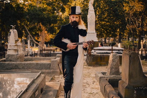 man standing in cemetery holding a banjo