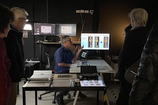man speaking to group while sitting at digitisation equipment