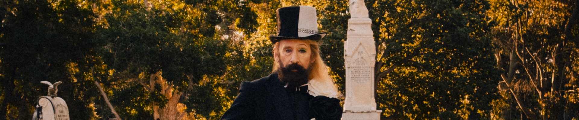 man standing in cemetery holding a banjo