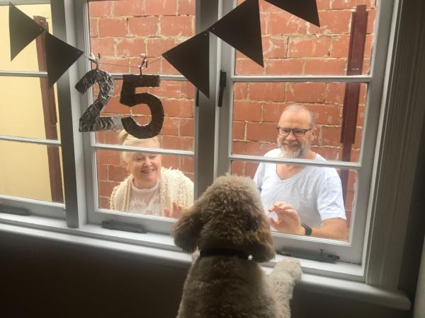 Neighbours wave through a window to pass on birthday celebrations during the COVID-19 pandemic