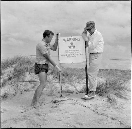 Two men with a sign warning of nuclear radiation Montebello Islands Western Australia 1956