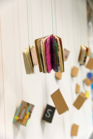 A line of books hanging from the roof via strings at the 2024 Sketchbook Project exhibition