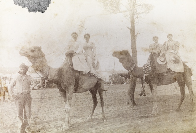 An Afghan cameleer leads two camels with women riding probably in Coolgardie c 1895