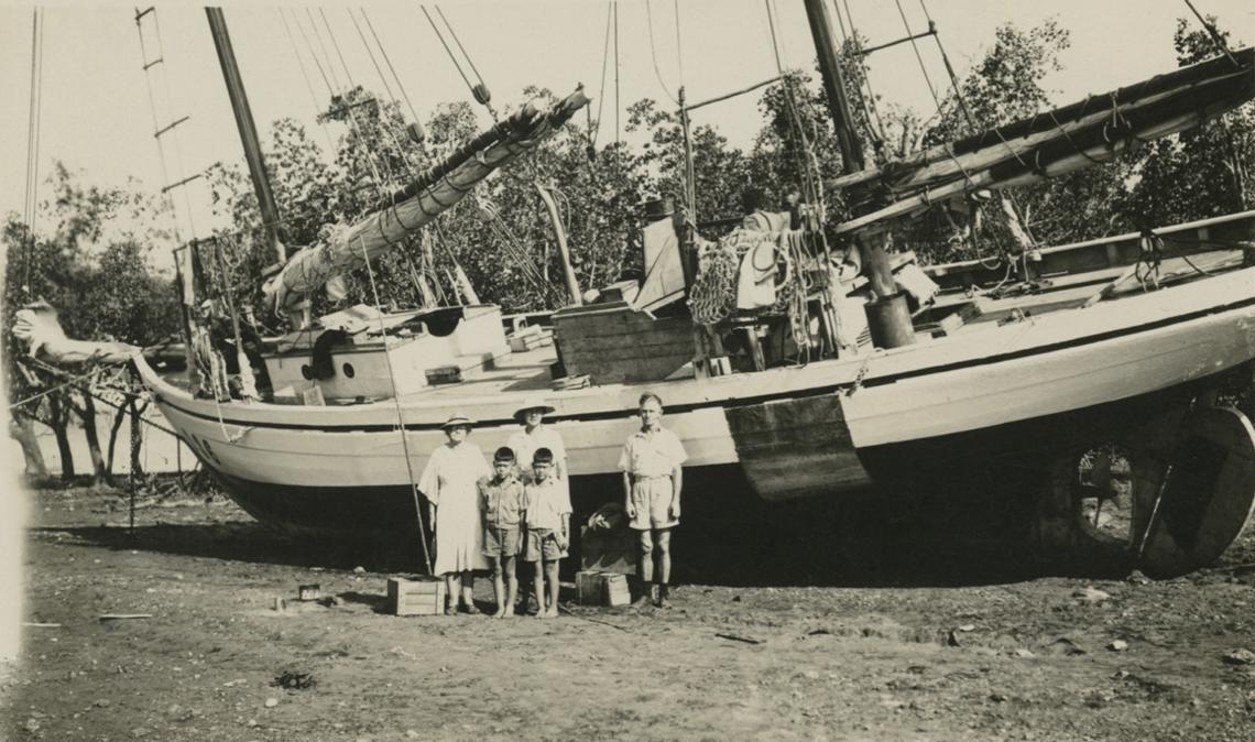 People standing in front of a lugger aground in sepia