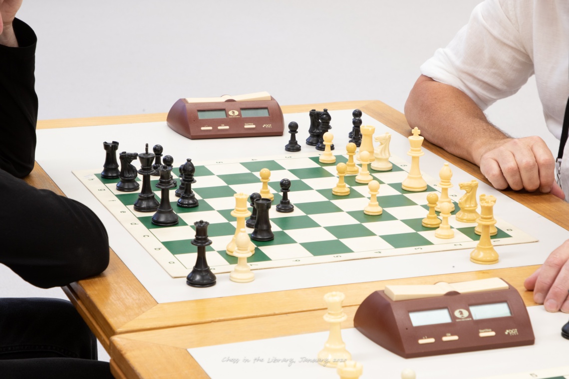 A chess board and a glimpse of two people sitting on either side