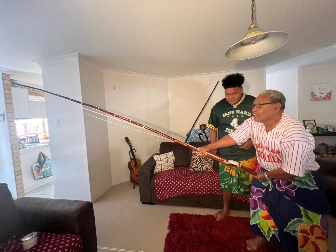 Fofo Poasa front showing his grandson Te Uluaki Poasa how to hold the traditional Tokelauan fishing rod kofe with the Pa Hi Atu skip jack tuna fishing lure 