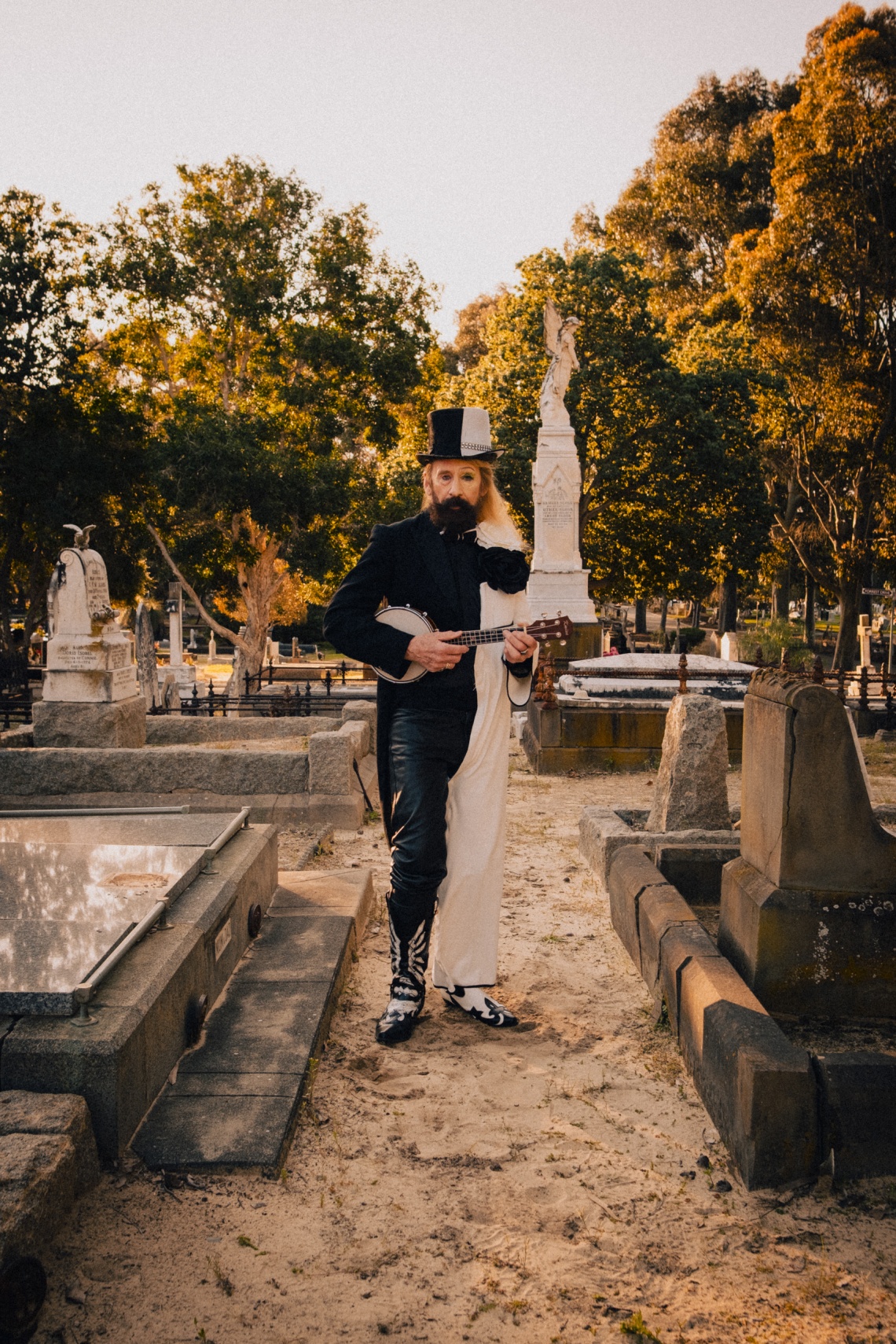 man standing in cemetery holding a banjo