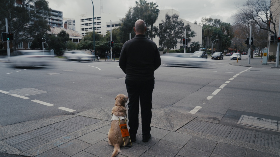 man and his guide dog facing a busy intersection