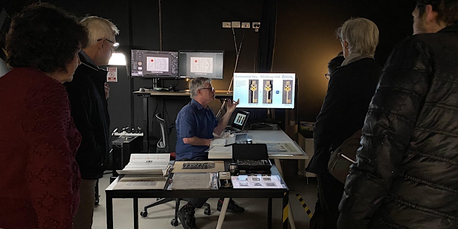 man speaking to group while sitting at digitisation equipment