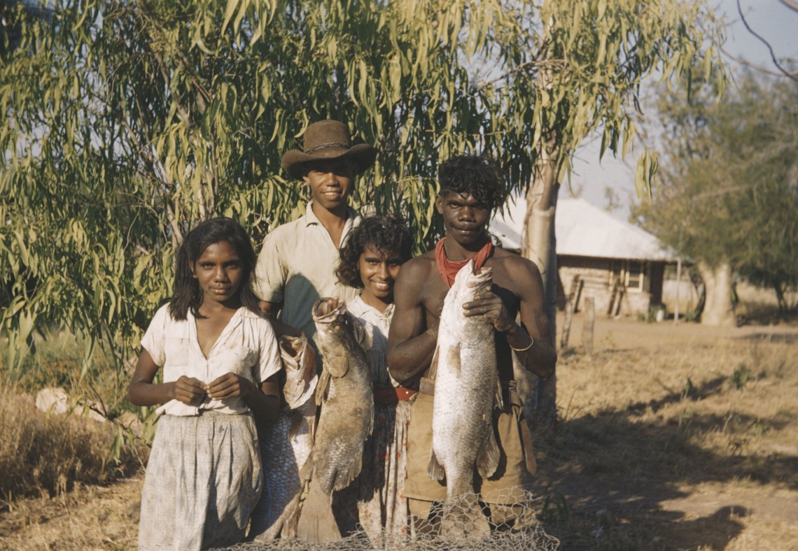 Four people look at the camera smiling two hold up big fish