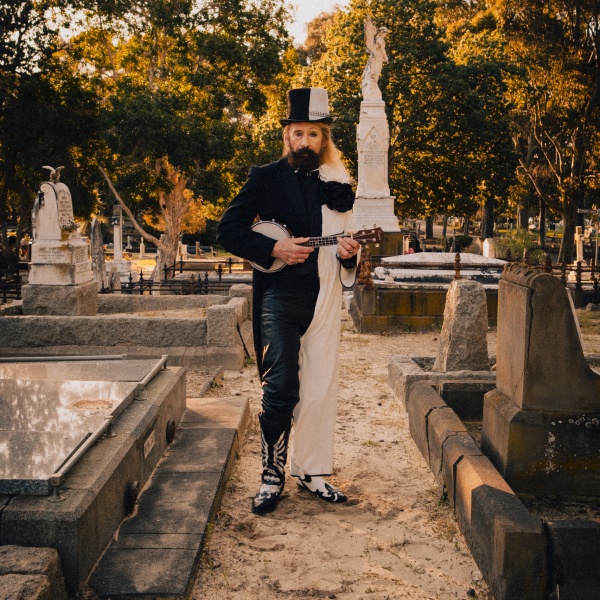 man standing in cemetery holding a banjo