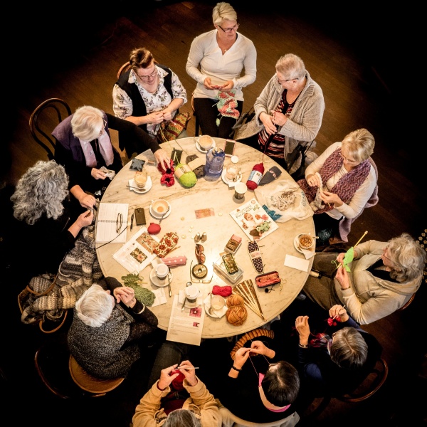A group of women sit around a table to knit poppies